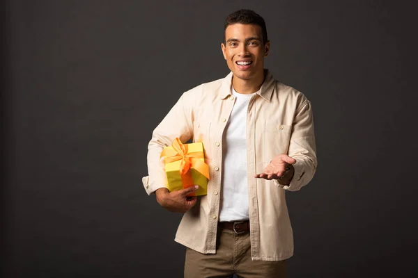 Homme mixte beau sourire en chemise beige avec la main tendue présente sur fond noir — Photo de stock