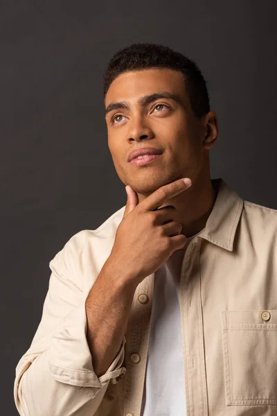 Pensive handsome mixed race man in beige shirt looking away on black background — Stock Photo