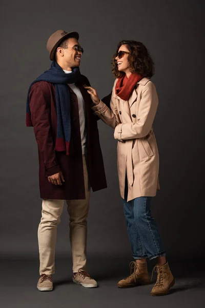 Happy stylish interracial couple in autumn outfit looking at each other on black background — Stock Photo