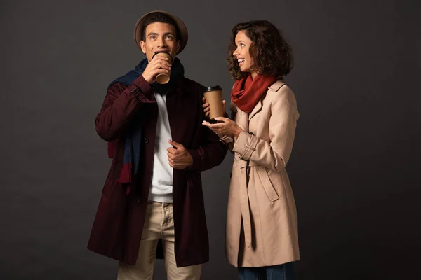 Sorrindo elegante casal interracial no outono roupa segurando café para ir e falando sobre fundo preto — Fotografia de Stock