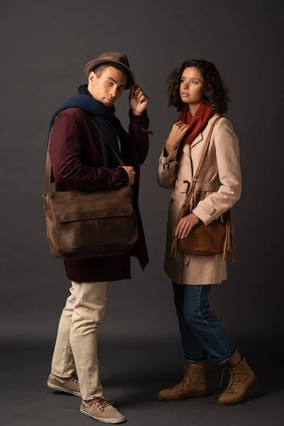 Pareja interracial con estilo en traje de otoño con bolsas sobre fondo negro - foto de stock