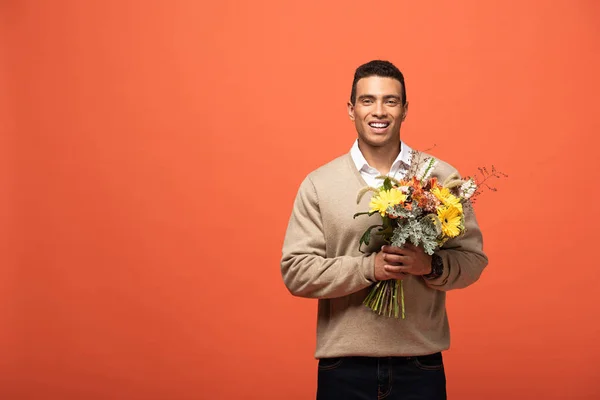 Uomo razza mista sorridente tenendo bouquet autunnale isolato su arancione — Foto stock