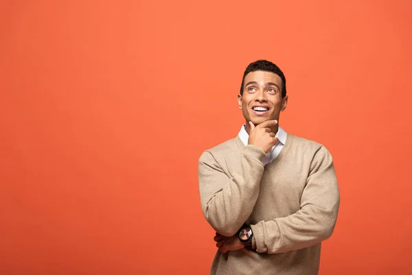 Dreamy mixed race man in beige sweater looking away isolated on orange — Stock Photo