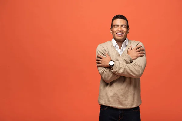 Happy mixed race man in beige sweater feeling cold isolated on orange — Stock Photo