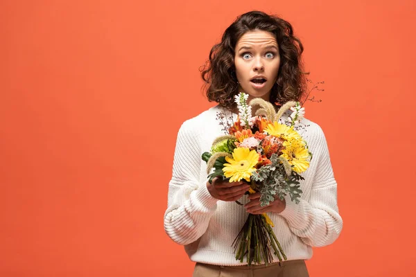 Mujer conmocionada en traje otoñal sosteniendo ramo de flores aisladas en naranja - foto de stock