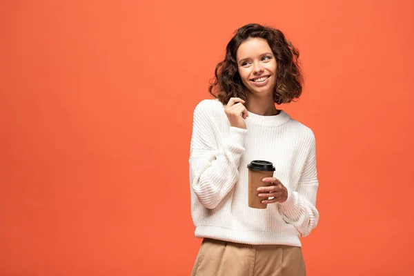 Souriant timide femme tenant café pour aller isolé sur orange — Photo de stock