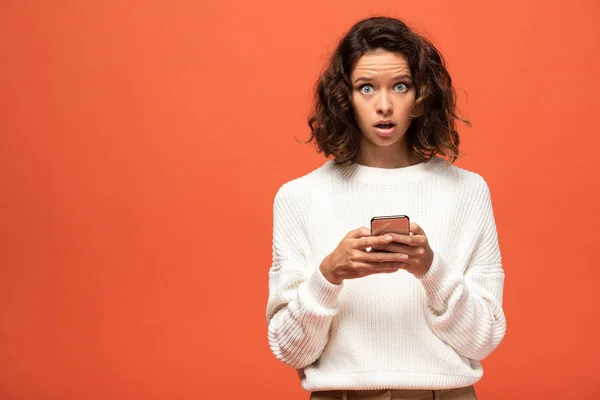 Shocked woman in autumnal outfit using smartphone isolated on orange — Stock Photo