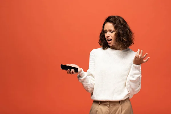 Verärgerte Frau im herbstlichen Outfit hält Smartphone mit leerem Bildschirm isoliert auf Orange — Stockfoto