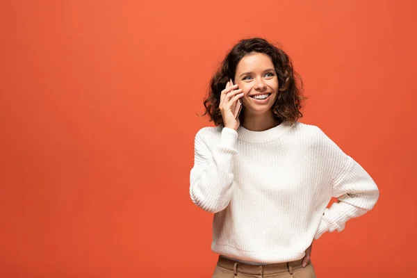 Mujer rizada feliz hablando en el teléfono inteligente aislado en naranja - foto de stock