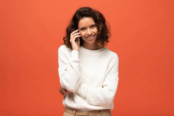 Mujer rizada feliz hablando en el teléfono inteligente aislado en naranja - foto de stock