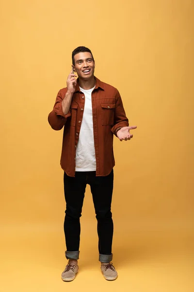 Sonriente hombre de raza mixta hablando en el teléfono inteligente aislado en amarillo - foto de stock