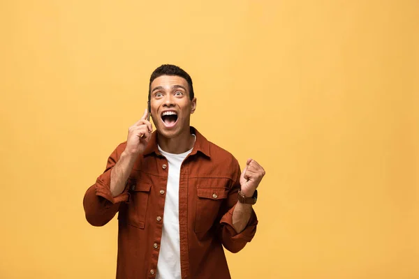 Homem de raça mista feliz falando no smartphone e mostrando sim gesto isolado no amarelo — Fotografia de Stock