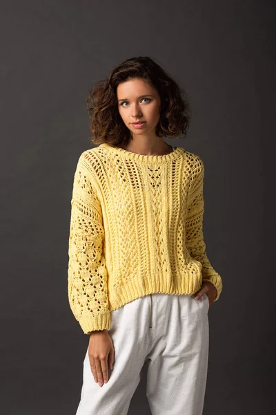 Curly woman in yellow sweater with hand in pocket on black background — Stock Photo