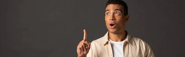 Panoramic shot of handsome mixed race man in beige shirt showing idea gesture on black background — Stock Photo