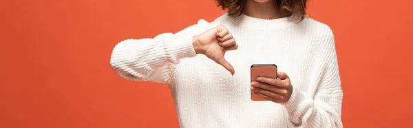 Cropped view of woman in autumnal outfit using smartphone and showing thumb down isolated on orange, panoramic shot — Stock Photo