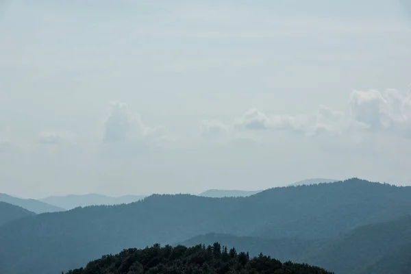 Weiße Wolken am Himmel in der Nähe von Bergen mit grünen Bäumen — Stockfoto