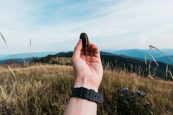 Vue recadrée de l'homme tenant un biscuit savoureux dans un champ près des montagnes — Photo de stock