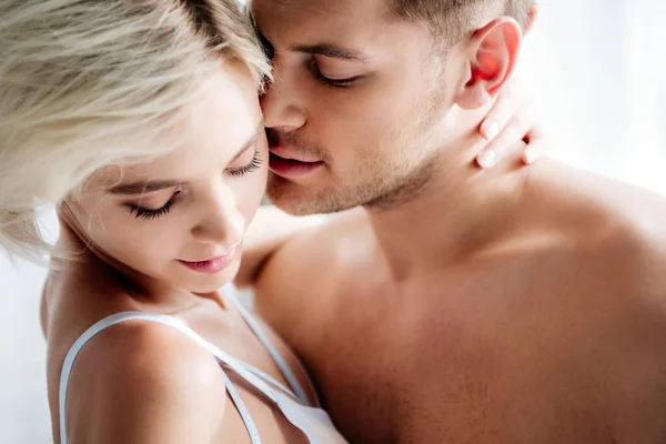 Handsome man kissing attractive and blonde woman in white underwear — Stock Photo