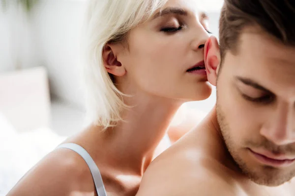 Selective focus of attractive and blonde woman kissing handsome man with closed eyes — Stock Photo