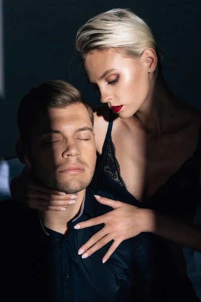 Привлекательная женщина в черном нижнем белье обнимает красивого мужчину в рубашке с закрытыми глазами — стоковое фото