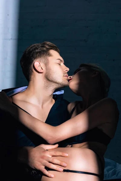 Mujer rubia en ropa interior negra besándose con un hombre guapo en camisa - foto de stock