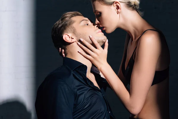 Привлекательная женщина в черном нижнем белье целует красивого мужчину в рубашке — стоковое фото