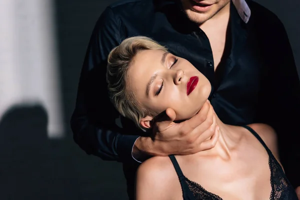 Vista recortada de hombre abrazando a mujer con los ojos cerrados en ropa interior negra - foto de stock