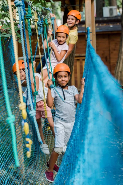 Selektiver Fokus fröhlicher multikultureller Kinder in Helmen in Seilnähe — Stockfoto