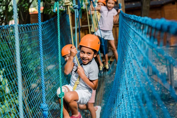 Selective focus of smiling african american kid in helmet climbing with friends — Stock Photo