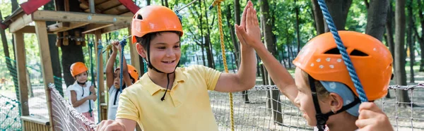 Panoramic shot of smiling kids giving high five near multicultural fiends — Stock Photo