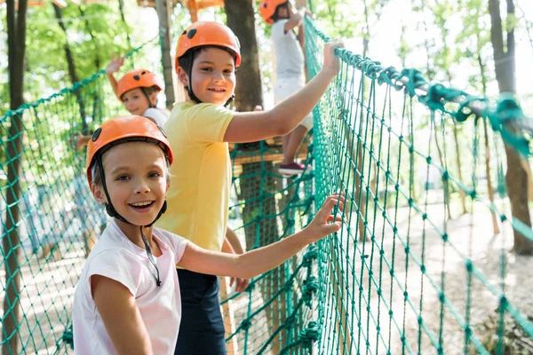 Selective focus of cheerful and cute kid on high rope trail with multicultural friends — Stock Photo