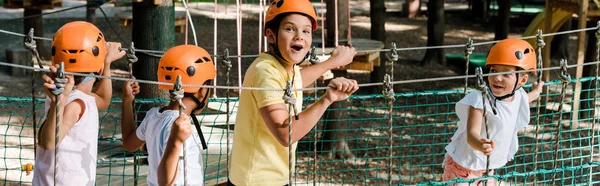 Panoramic shot of surprised boy near cute multicultural friends in helmets — Stock Photo