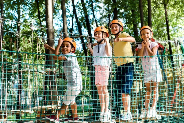 Chicos multiculturales felices cerca de amigos en cascos en el parque de aventuras - foto de stock
