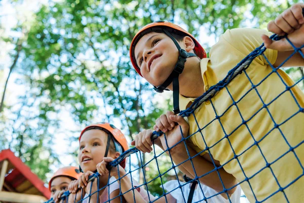 Baixo ângulo vista de crianças sorridentes em capacetes laranja menino feliz no parque de aventura — Fotografia de Stock