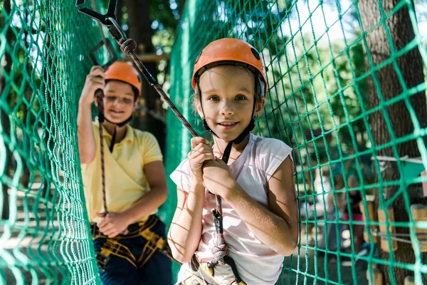 Messa a fuoco selettiva di bambini felici in caschi con attrezzature di altezza nel parco avventura — Foto stock