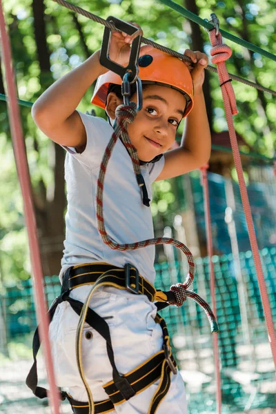 Selective focus of cute african american boy with height equipment on high rope trail — Stock Photo