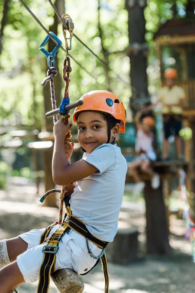 Enfoque selectivo de adorable niño afroamericano en casco naranja en parque de aventuras - foto de stock