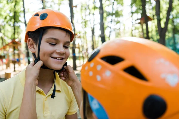 Cropped view of kid touching helmet of happy friend in adventure park — Stock Photo