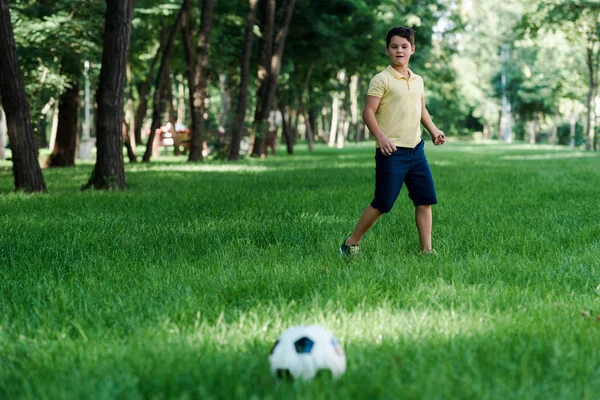 Selective focus of cute boy looking at football on grass — Stock Photo