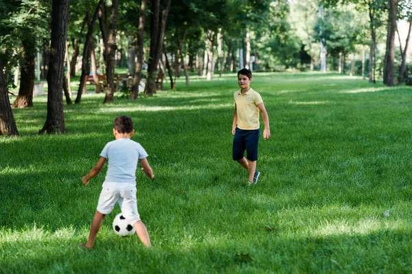 Милые мультикультурные мальчики играют в футбол на траве — стоковое фото