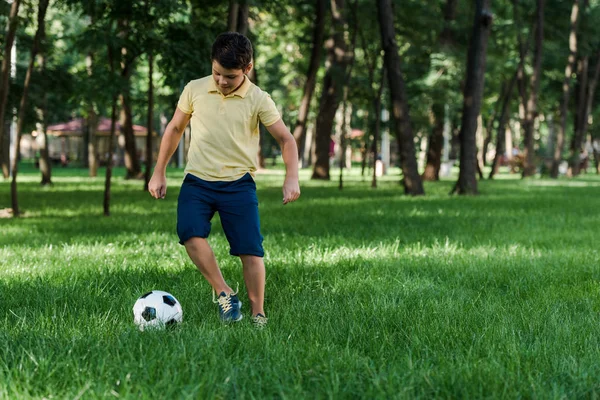 Хлопчик грає у футбол на зеленій траві в парку — стокове фото