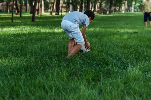 Enfoque selectivo de niño afroamericano de pie cerca de la pelota en la hierba - foto de stock