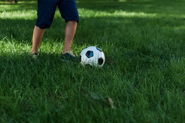 Vue recadrée du garçon jouant au football sur l'herbe verte — Photo de stock