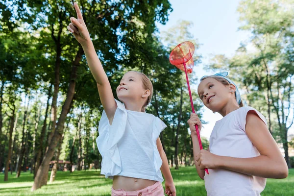 Carino bambino punta con dito vicino amico felice con rete farfalla — Foto stock