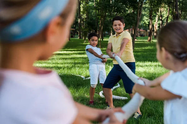 Selective focus of happy multicultural kids competing in tug of war outside — Stock Photo
