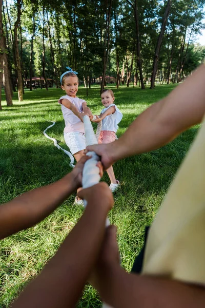 Cropped view of multicultural children competing in tug of war with cute friends outside — Stock Photo