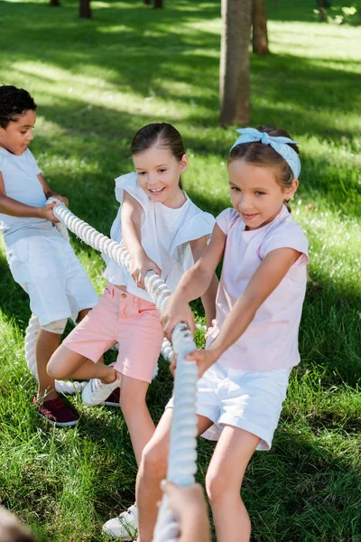 Selective focus of happy multicultural children competing in tug of war — Stock Photo