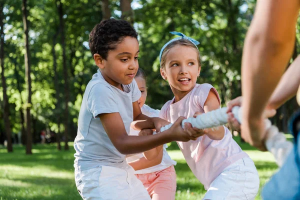 Vista recortada de niño compitiendo en tira y afloja con amigos multiculturales - foto de stock