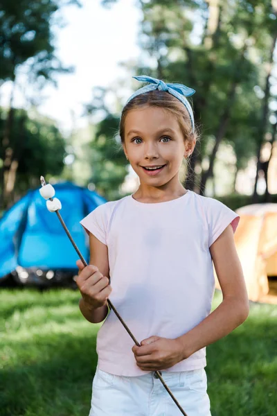 Surprised child smiling while holding stick with sweet marshmallows — Stock Photo