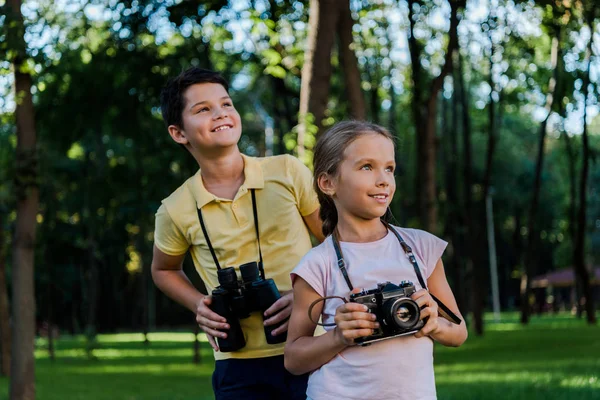 Niños felices mirando hacia arriba mientras sostienen prismáticos en el parque - foto de stock